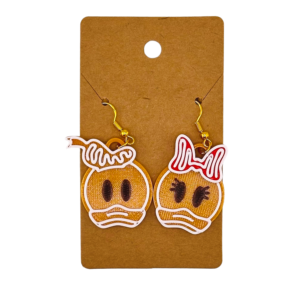 Gingerbread-shaped donald and daisy earrings on a brown card with a white background