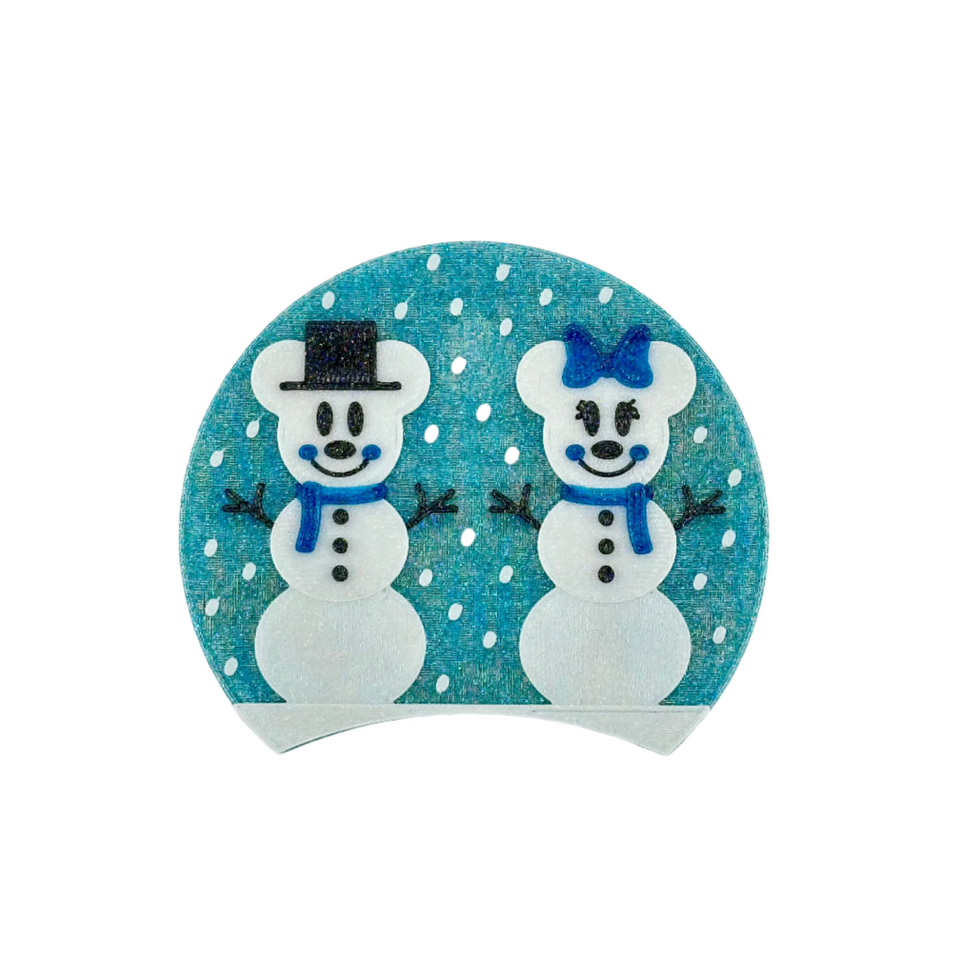 The Snow Mice Couple sits on a bed of snow with snow falling in the background. One mouse snowman has a top hat and scarf, the other has a bow a scarf.